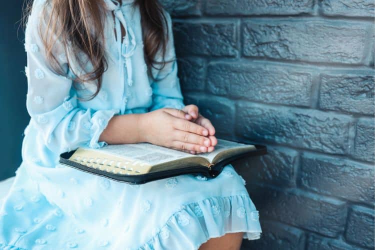 little girl's hands folded over a Bible