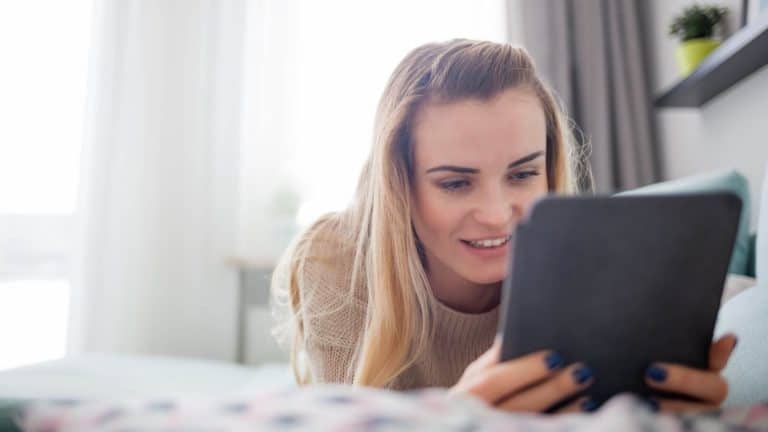 woman laying across a bed reading on an ereader