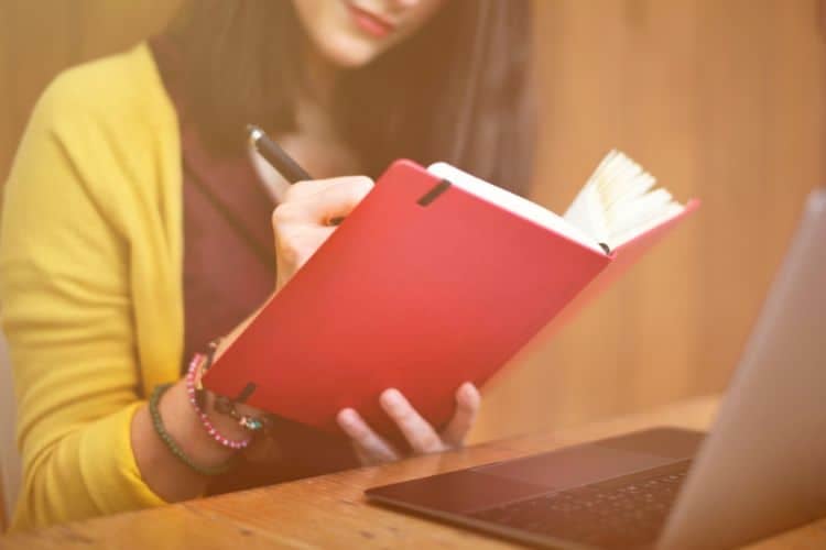 woman writing a prayer list in a red notebook