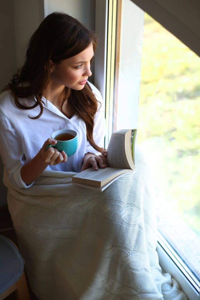 woman reading her Bible while drinking coffee in front of a window