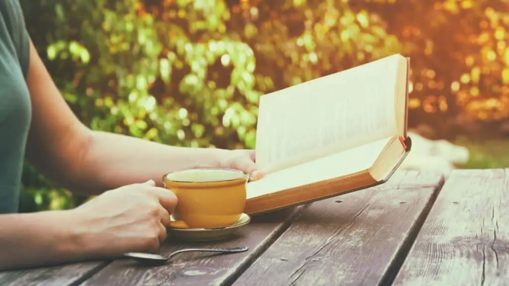 woman reading her Bible and drinking coffee outdoors in the fall