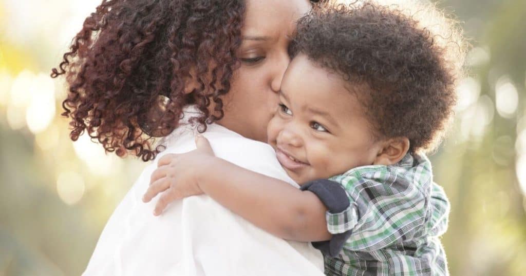 stay-at-home mom holding her toddler son and kissing him on the cheek