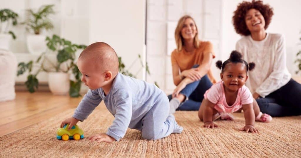 two stay-at-home moms smiling while watching babies playing on the floor