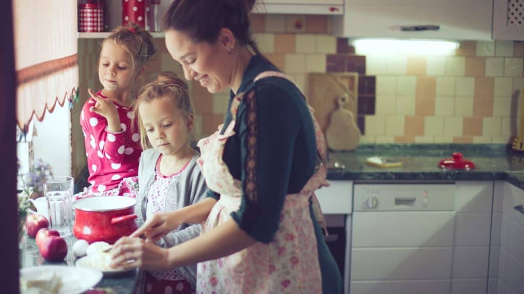 mom wearing an apron preparing food with her two young daughters