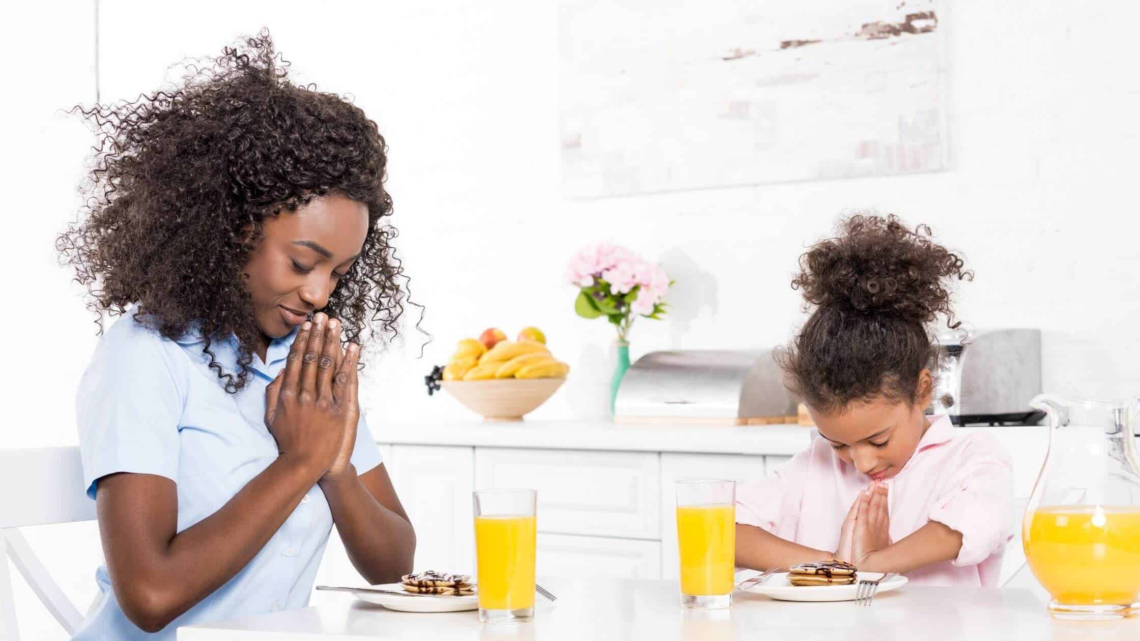 woman and her daughter praying at the breakfast table