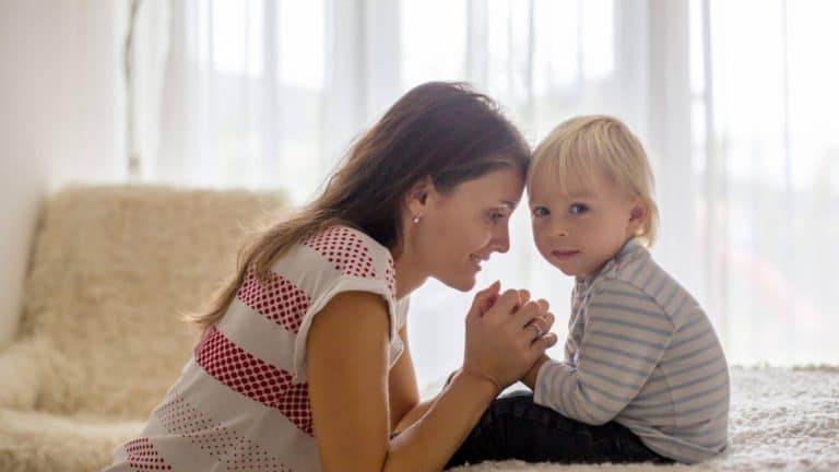 mother kneeling her bed praying with a little boy