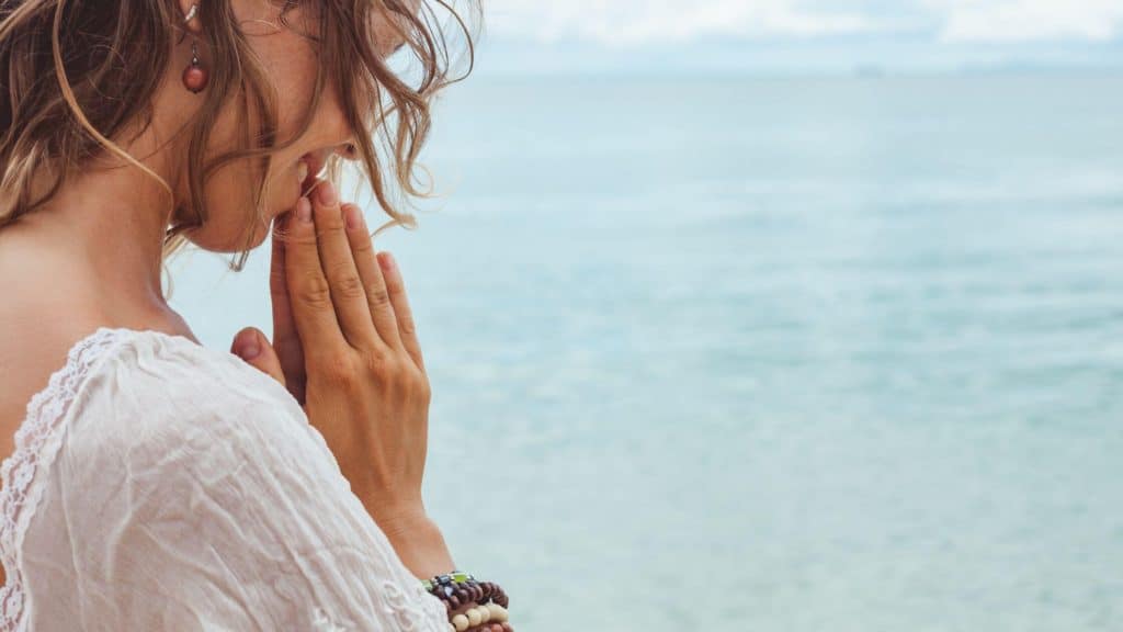 partial side view of woman with hand clasped in prayer beside the ocean