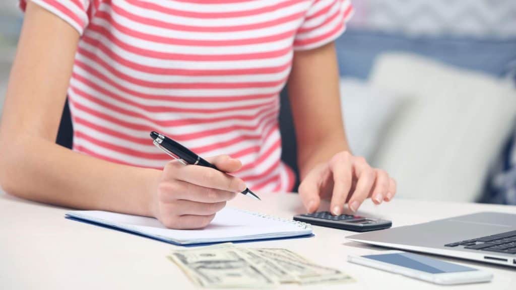 close-up of womans hands with a pencil, calculator and money 