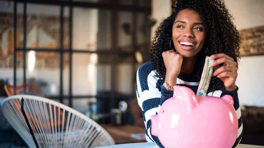 smiling woman putting money into a piggy bank