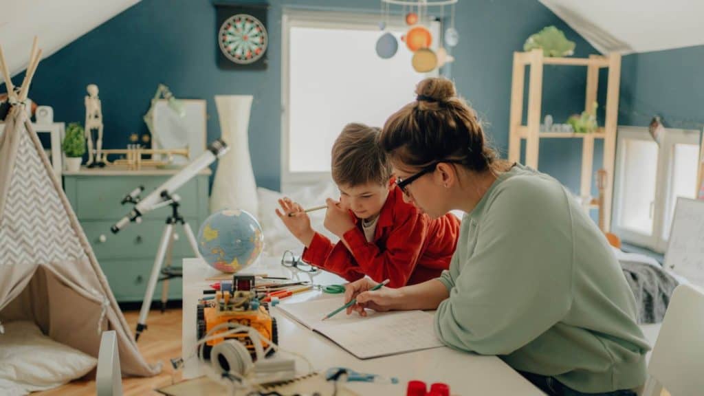mother helping her son with homeschool in a bedroom setting surrounded by educational toys and games