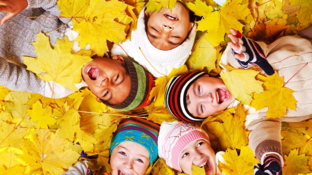 smiling kids covered in autumn leaves