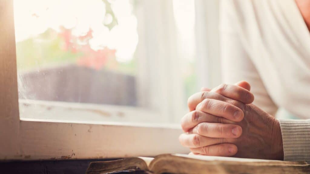 woman's praying hands clasped over an open Bible