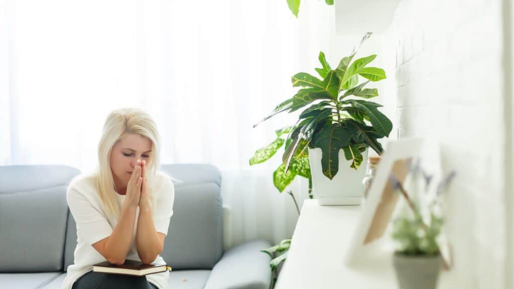 woman sitting on a couch with hands clasped in prayer