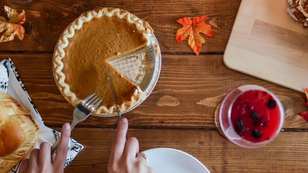 woman's hands cutting a pumpkin pie