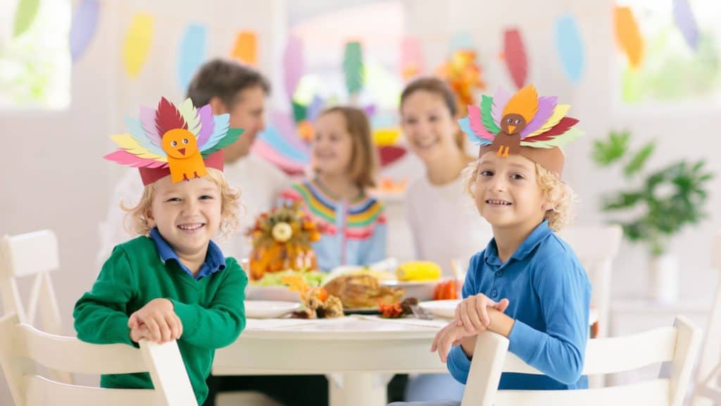 smiling children at a Thanksgiving table wearing feather hats