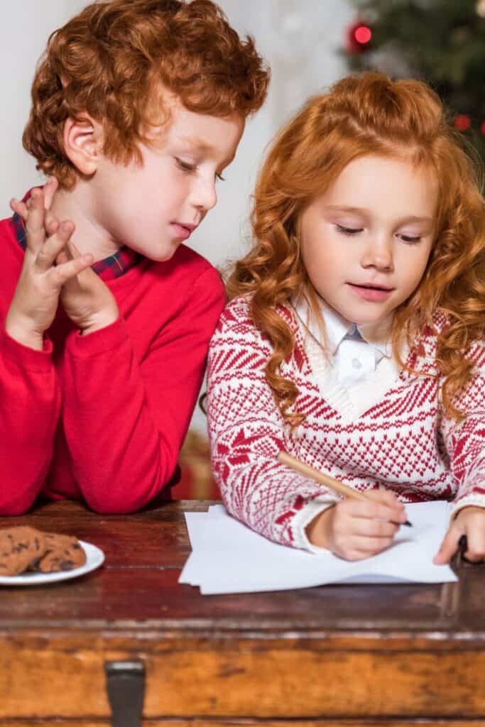 boy and girl in Christmas sweaters writing a letter