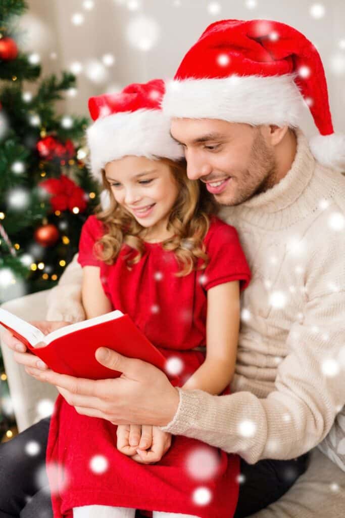 man wearing a Santa hat reading to a little girl also wearing a Santa hat