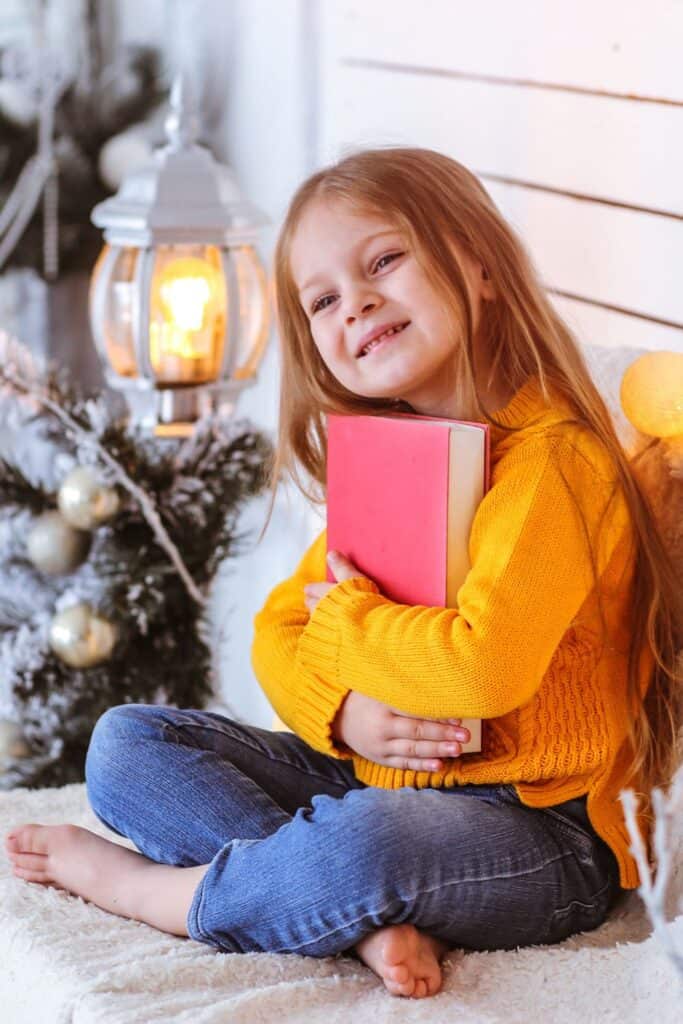 little girl holding a book in front of a Christmas tree