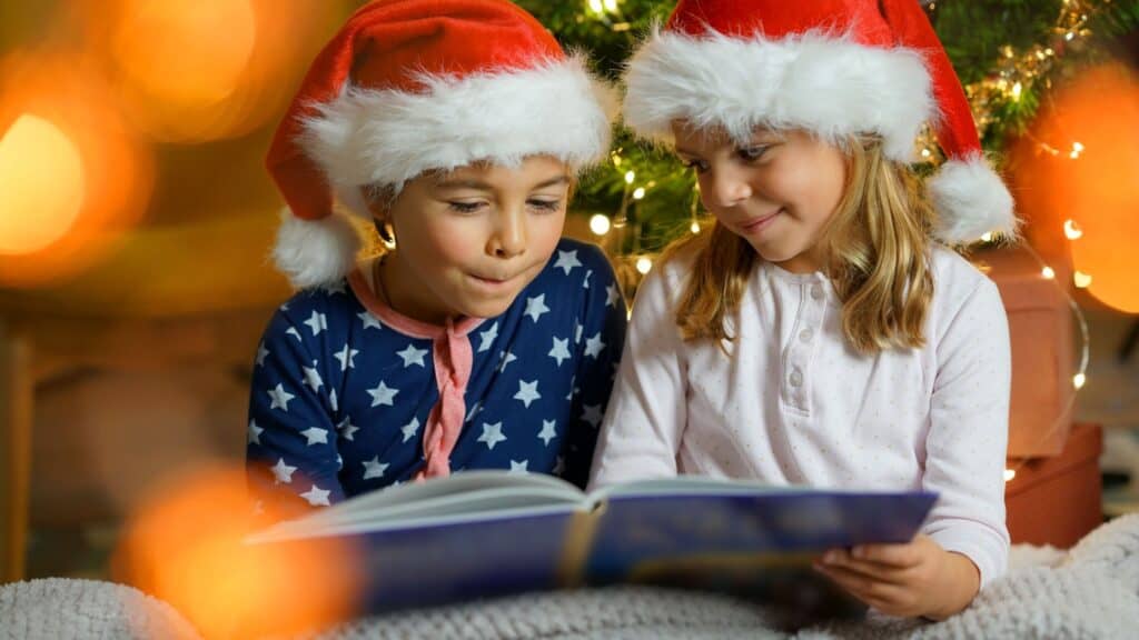 a boy and girl wearing Santa hats and reading a Christmas book