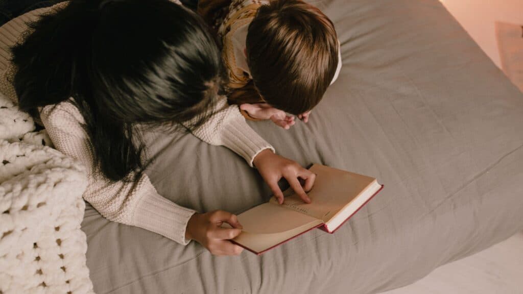 mother and child reading the Bible together lying on a bed