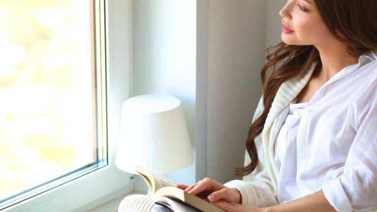 woman reading her Bible beside a window in the morning