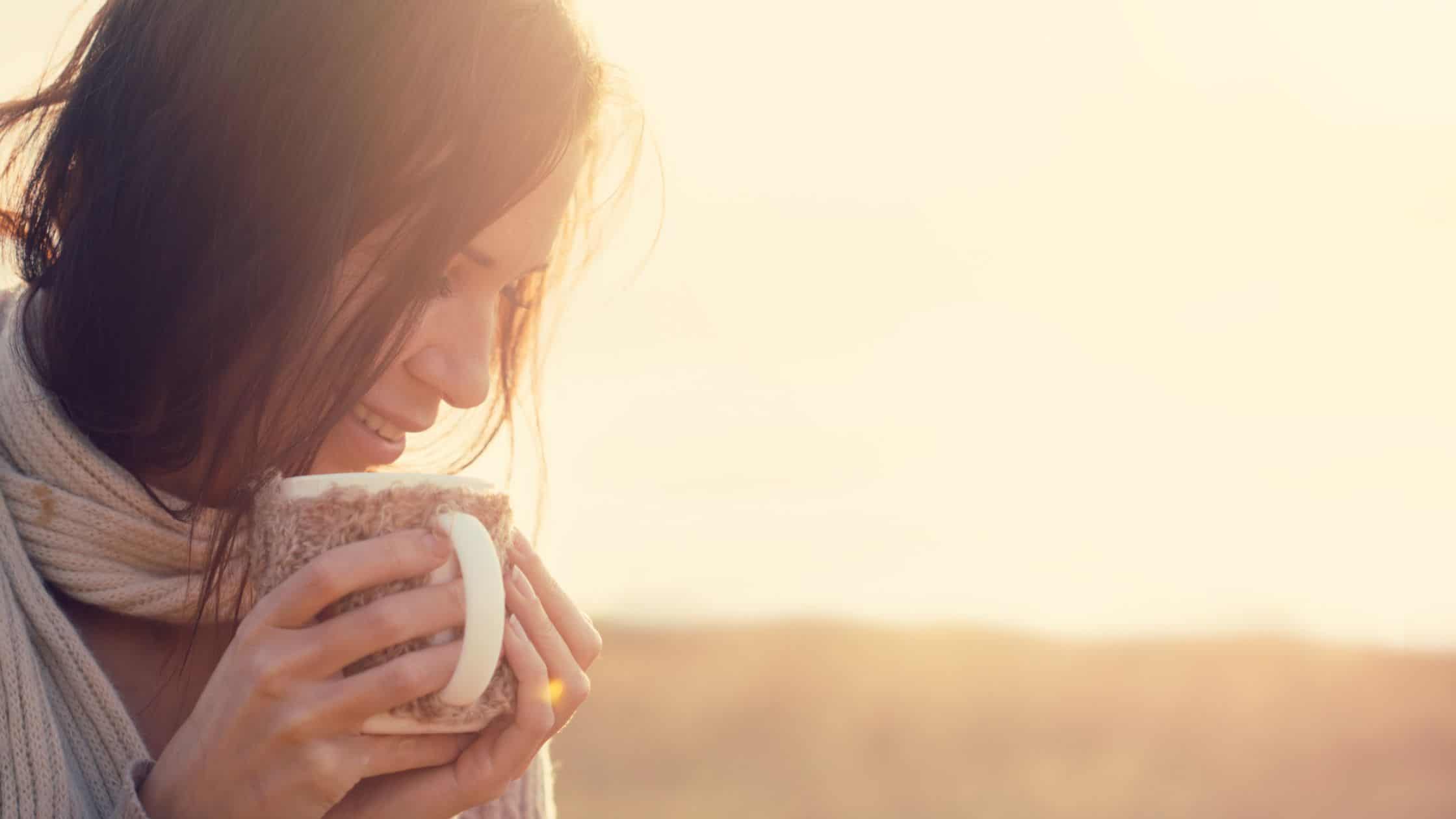 smiling woman with cup of coffee outdoors in the early morning