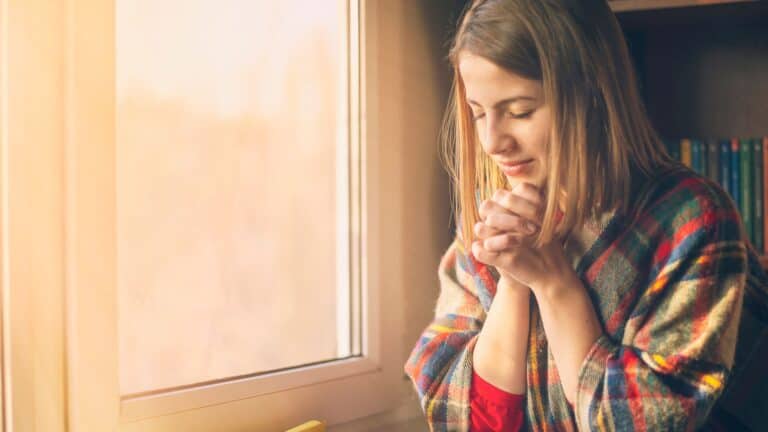 woman praying in front of a window in the morning