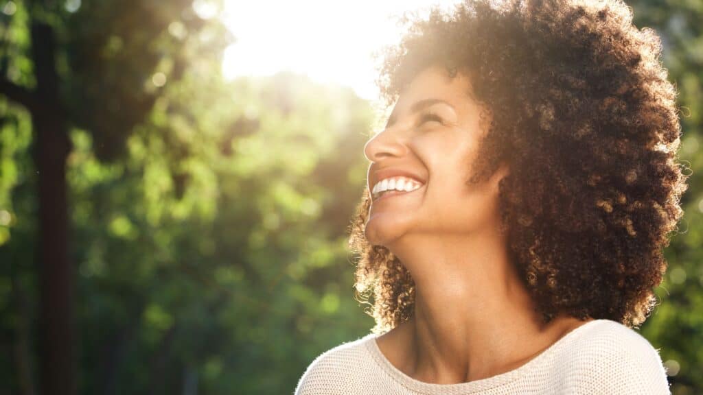 smiling woman with sunlight shining through the trees in the background