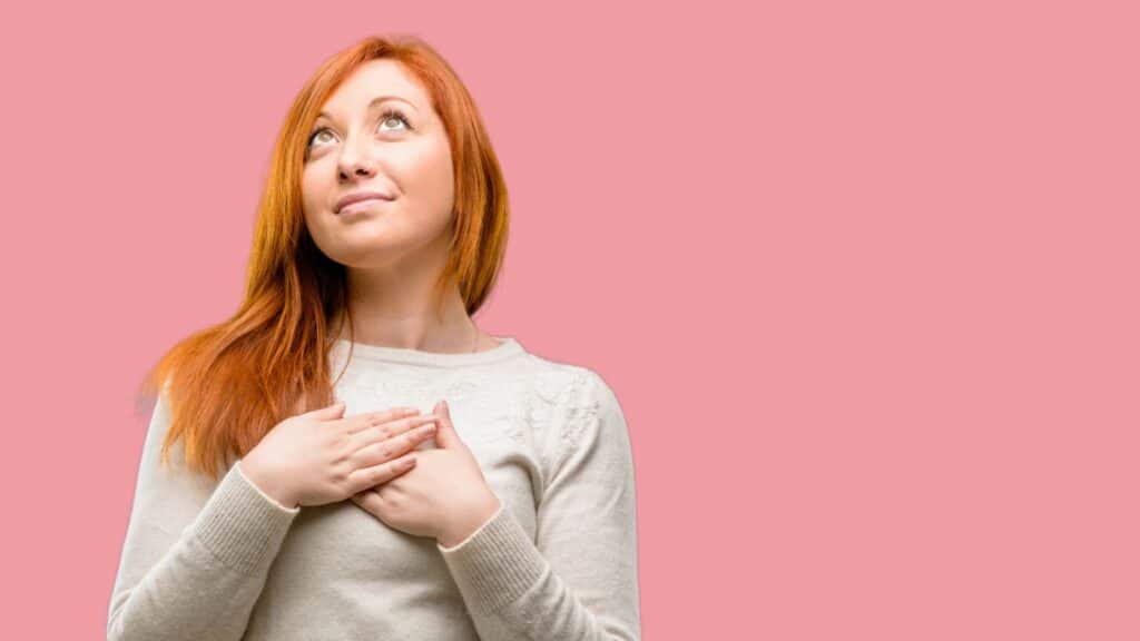 woman standing with hands clasped over her heart