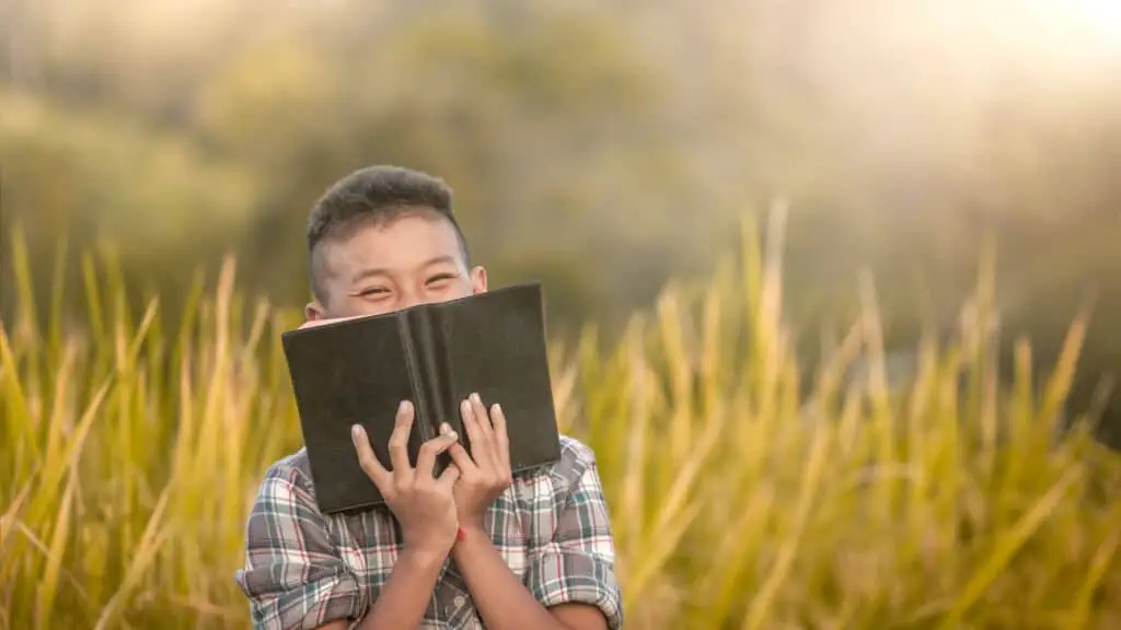 smiling young boy holding a Bible in a field