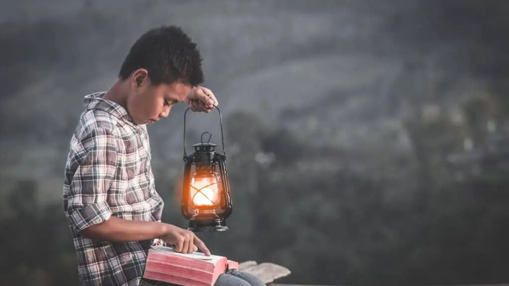 boy reading his Bible in the semi-darkness while holding a lantern