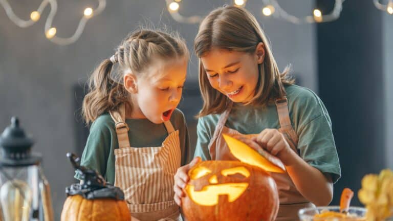 young girls looking inside a well-lit jack-o-lantern at halloween