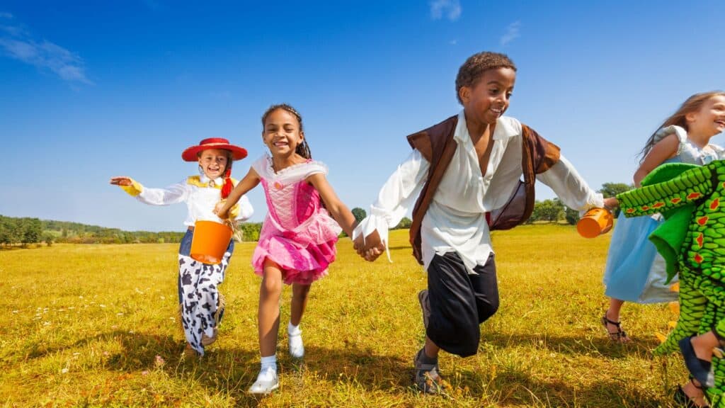 kids running through a field outdoors dressed in Halloween costumes