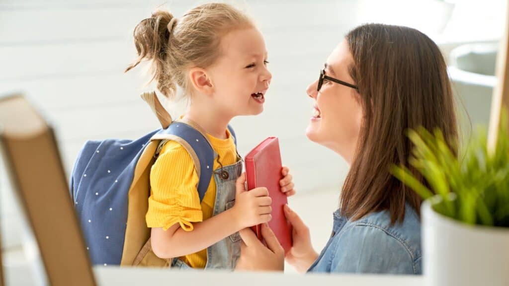 woman giving a Bible to a little girl wearing a yellow shirt and carrying a backpack