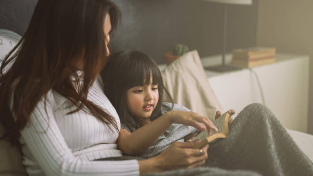 woman reading with her daughter while covered with a blanket in bed