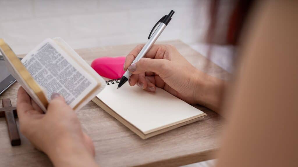 woman writing a passage from her Bible into a notebook