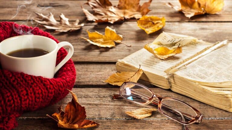 open Bible with fall leaves and a cup of coffee on a table covered with leaves