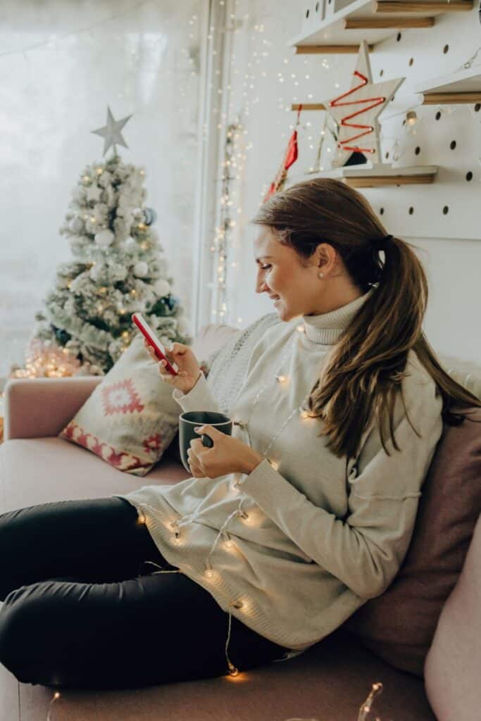 woman sitting beside a Christmas tree drinking a mug of warm drink