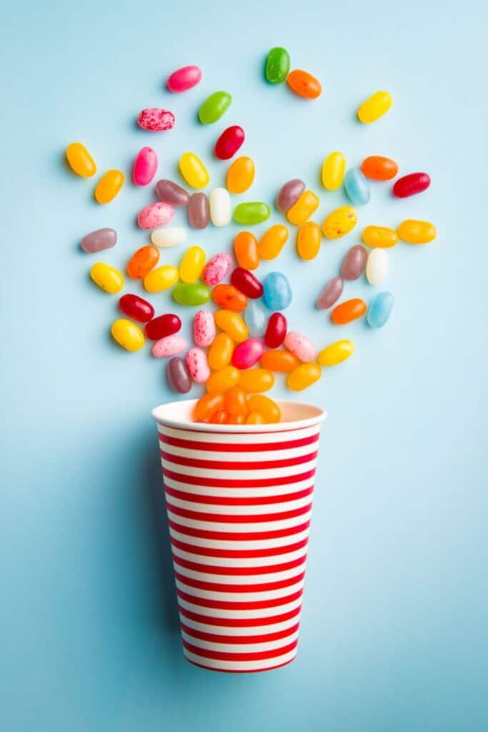 cup spilling colorful jelly beans on a light blue background