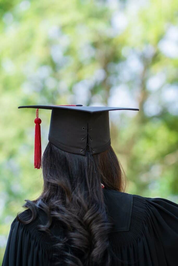 young woman wearing a black graduation cap and gown facing away from the camera