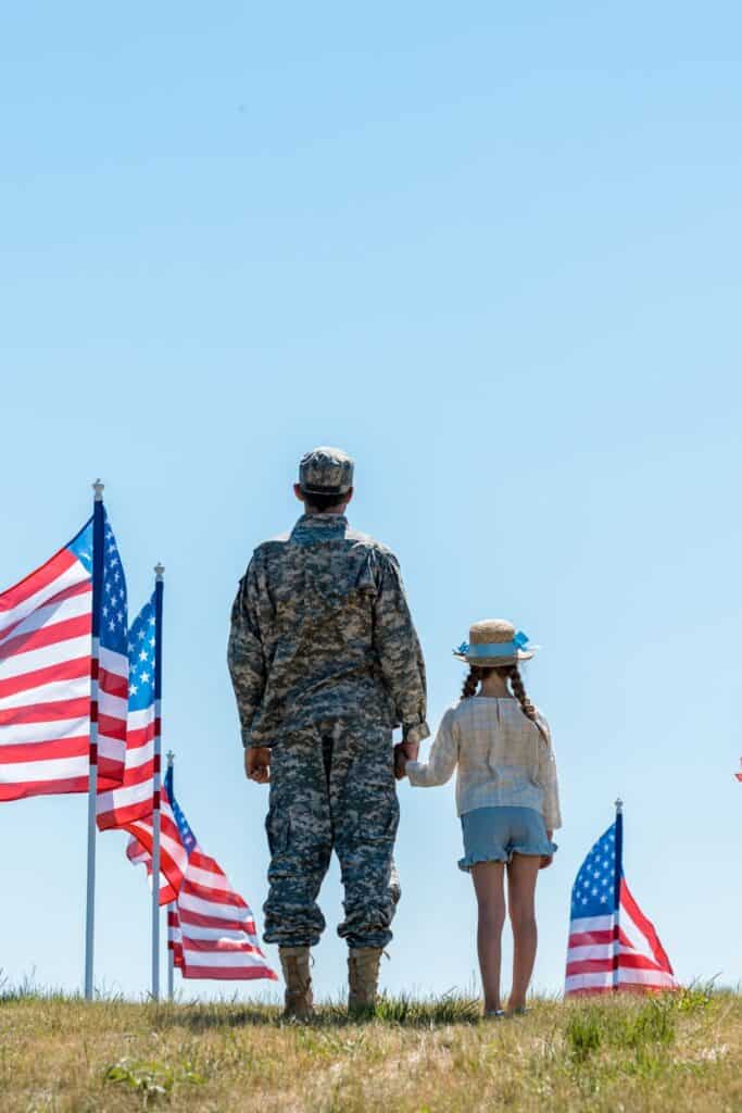 man wearing a military uniform holding hands with a little girl while standing in the middle of a display of American flags