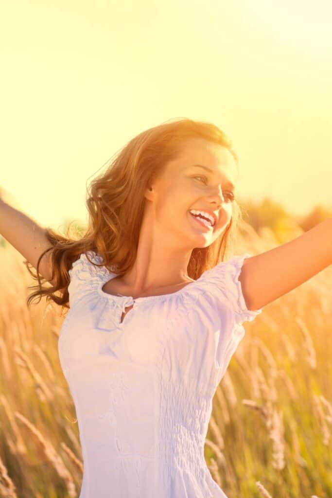 confident young woman with arms raised in a field