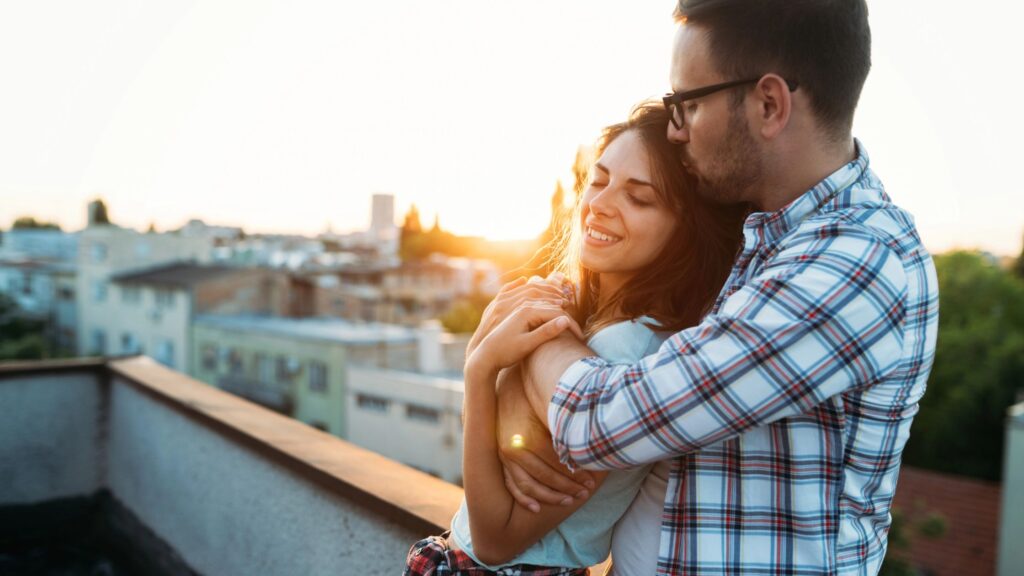 husband and wife hugging with a city scene in the background