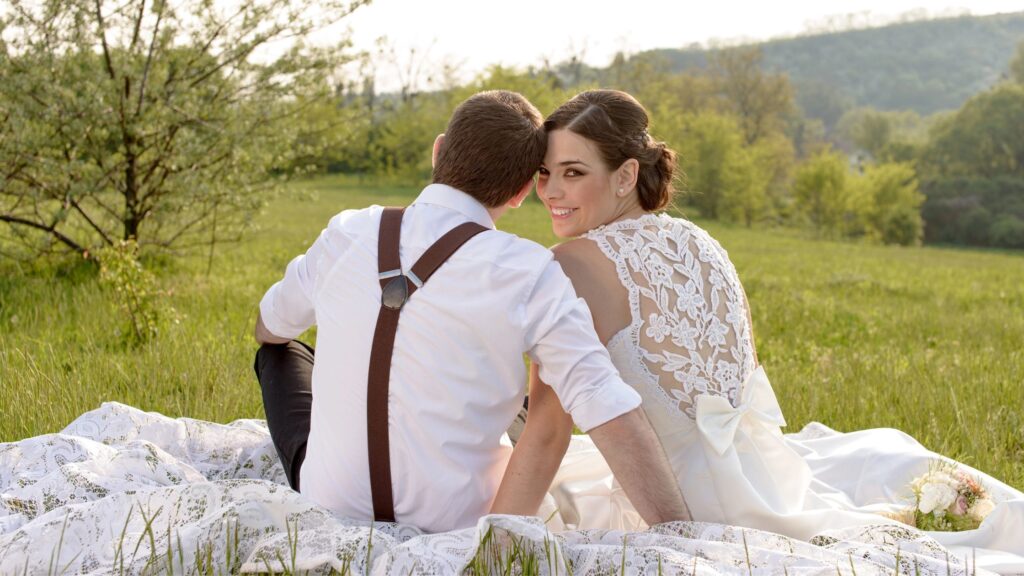 bride and groom sitting on the grass facing away from the camera