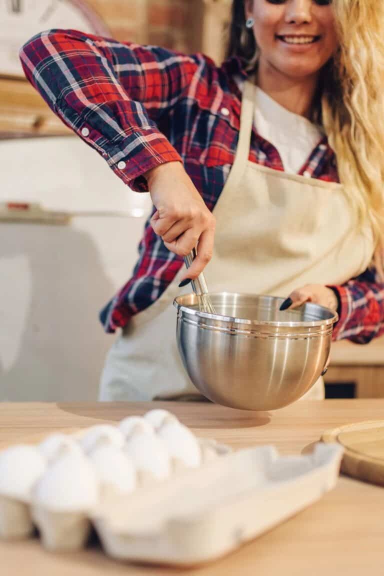 woman stirring food in an aluminum bowl with a carton of eggs in the foreground