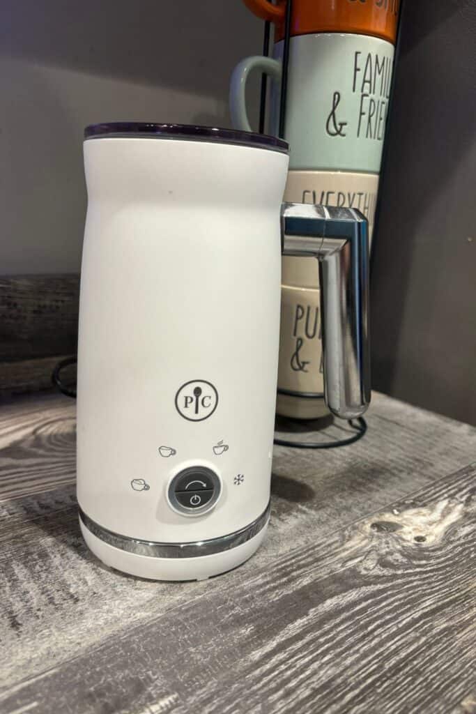 white electric milk frother on a kitchen counter with coffee mugs in the background