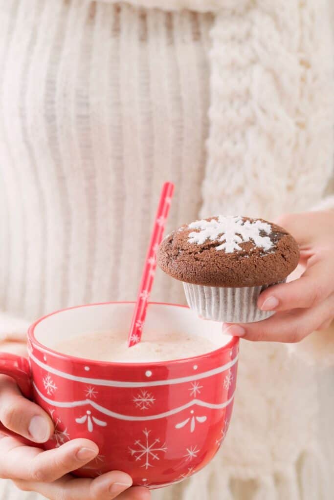 woman's hands holding a cup of cocoa and a cupcake