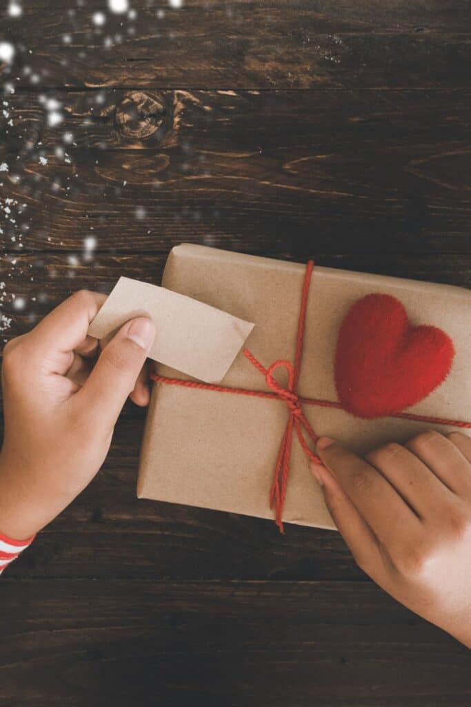 hands untying a ribbon on top of a present with a heart on it