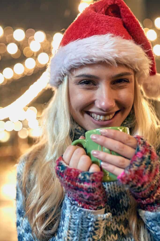 smiling woman holding a mug in her hands while wearing a santa hat