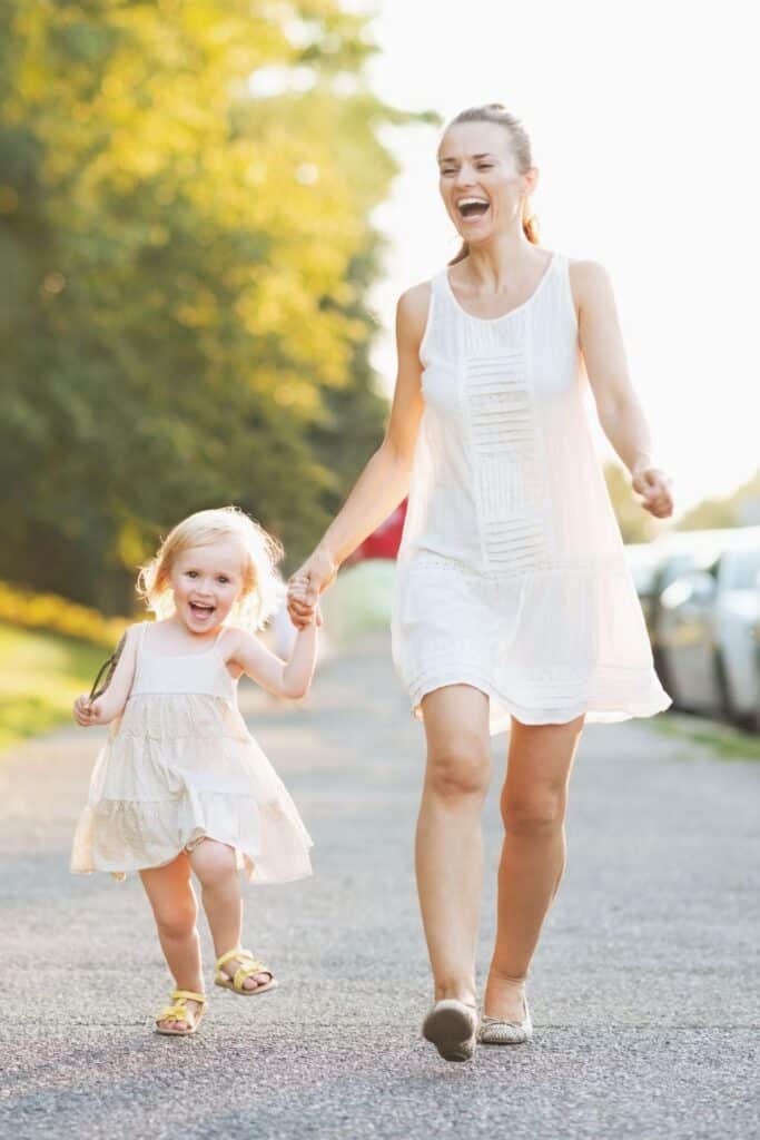 woman holding hands with a little girl and walking on a road